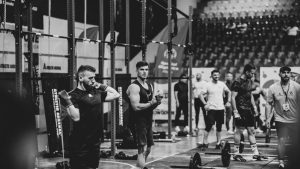 Black and white image of a fitness competition showcasing athletes and weights in a gym setting.